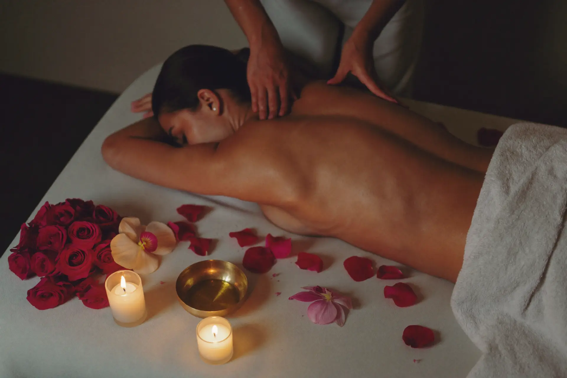 Woman receiving a massage surrounded by candles, rose petals and orchids